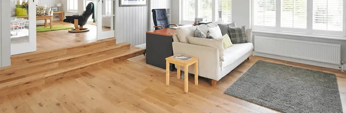 A modern living room with professionally installed laminate flooring, a beige sofa, a small side table, a gray rug, and large windows with white shutters in Lakewood, CO